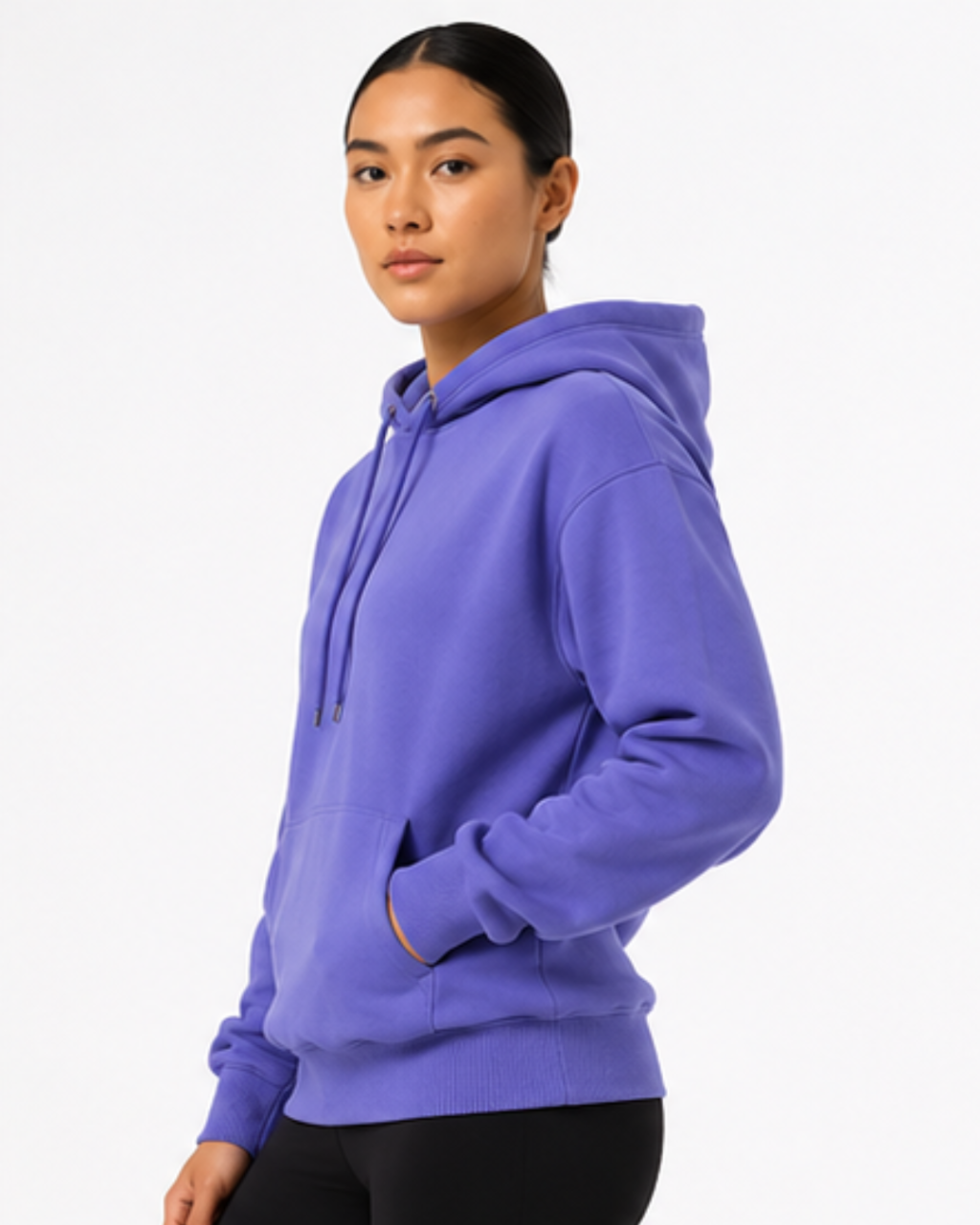 A woman wearing a solid purple pullover hoodie with black pants, photographed from a side profile against a clean white studio background.