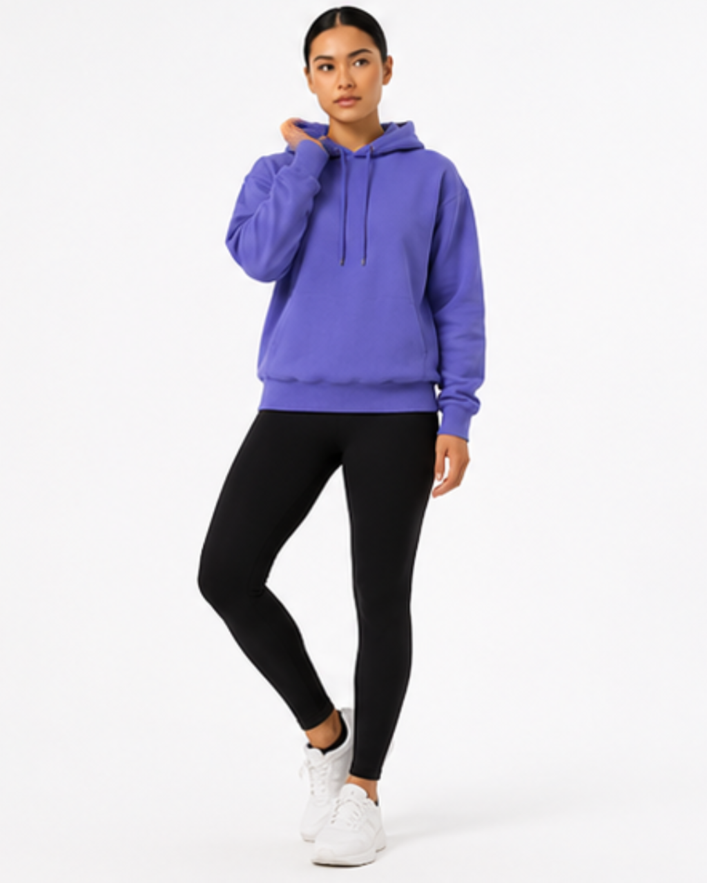 A woman modeling a purple pullover hoodie with black leggings and white sneakers against a plain white studio background.