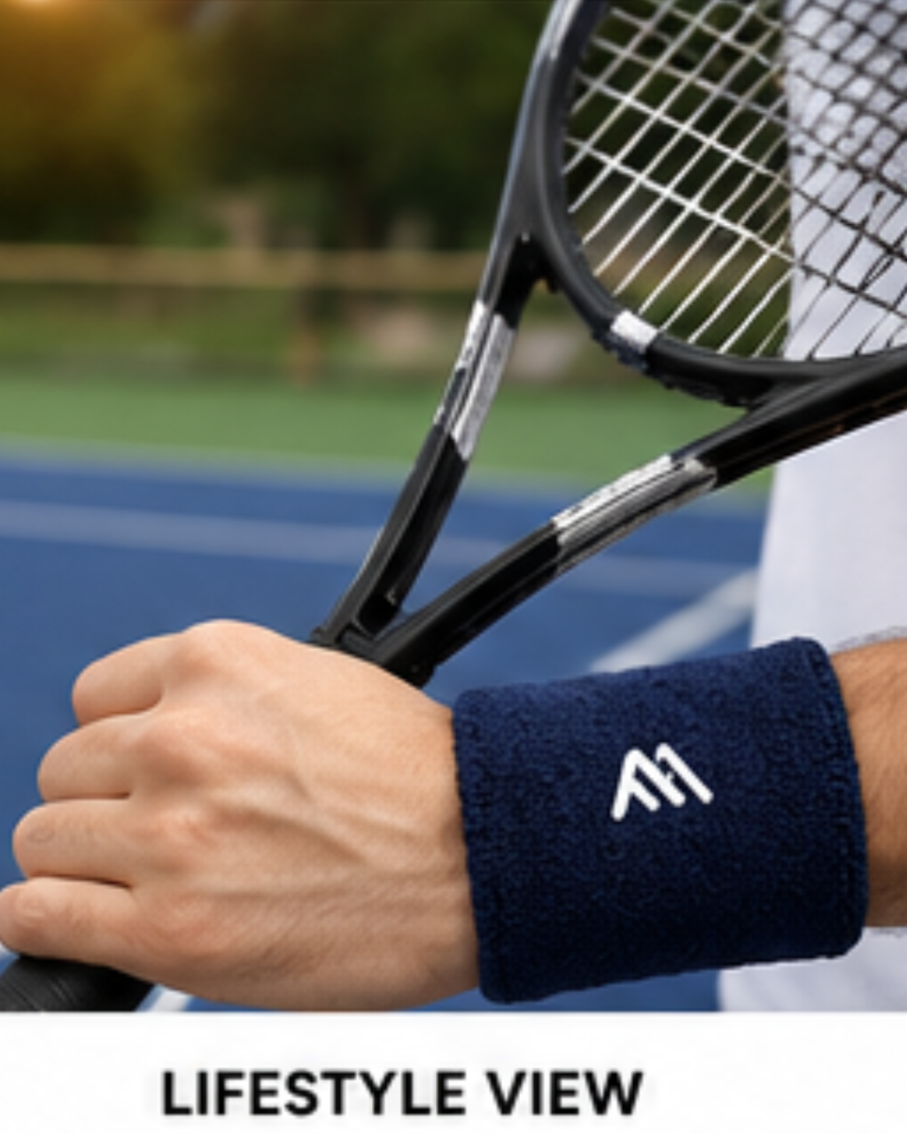 A close-up lifestyle shot of a person's hand holding a black tennis racket on an outdoor tennis court, wearing a navy blue terry cloth wristband with a white stylized 'M' logo. The text 'LIFESTYLE VIEW' is displayed at the bottom.